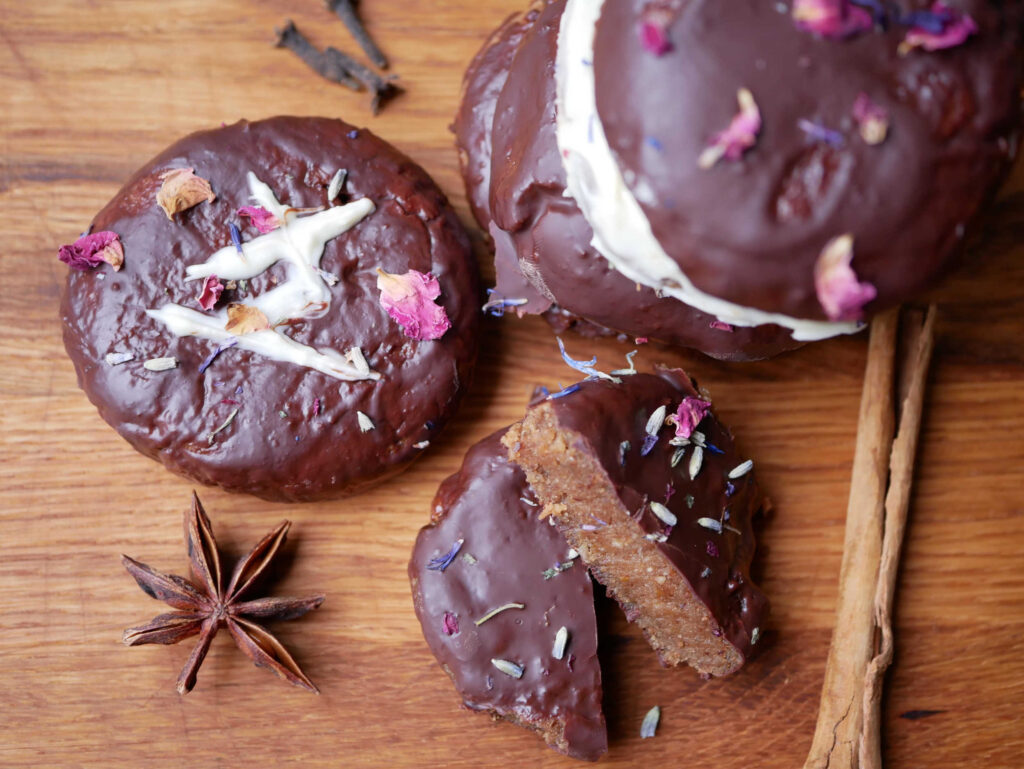 Auf dem Bild sind Lebkuchen mit dunkler und weißer Schokolade überzogen zu sehen. Sie lieben auf einem Brett. Der vordere Lebkuchen habt eine dunkle Glasuer und mit weißer Schokolade das TryHyggeYoga Logo stehen. Das Rezept ist ein tolles, saftiges und veganes Lebkuchenrezept mit ayurvedischen Gewürzen von TryHyggeYoga.